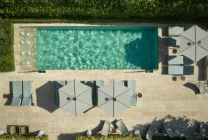 Aerial view of the Can Aulí pool: long and clear, lined in pale stone, with umbrellas and chairs around it on a stone terrace