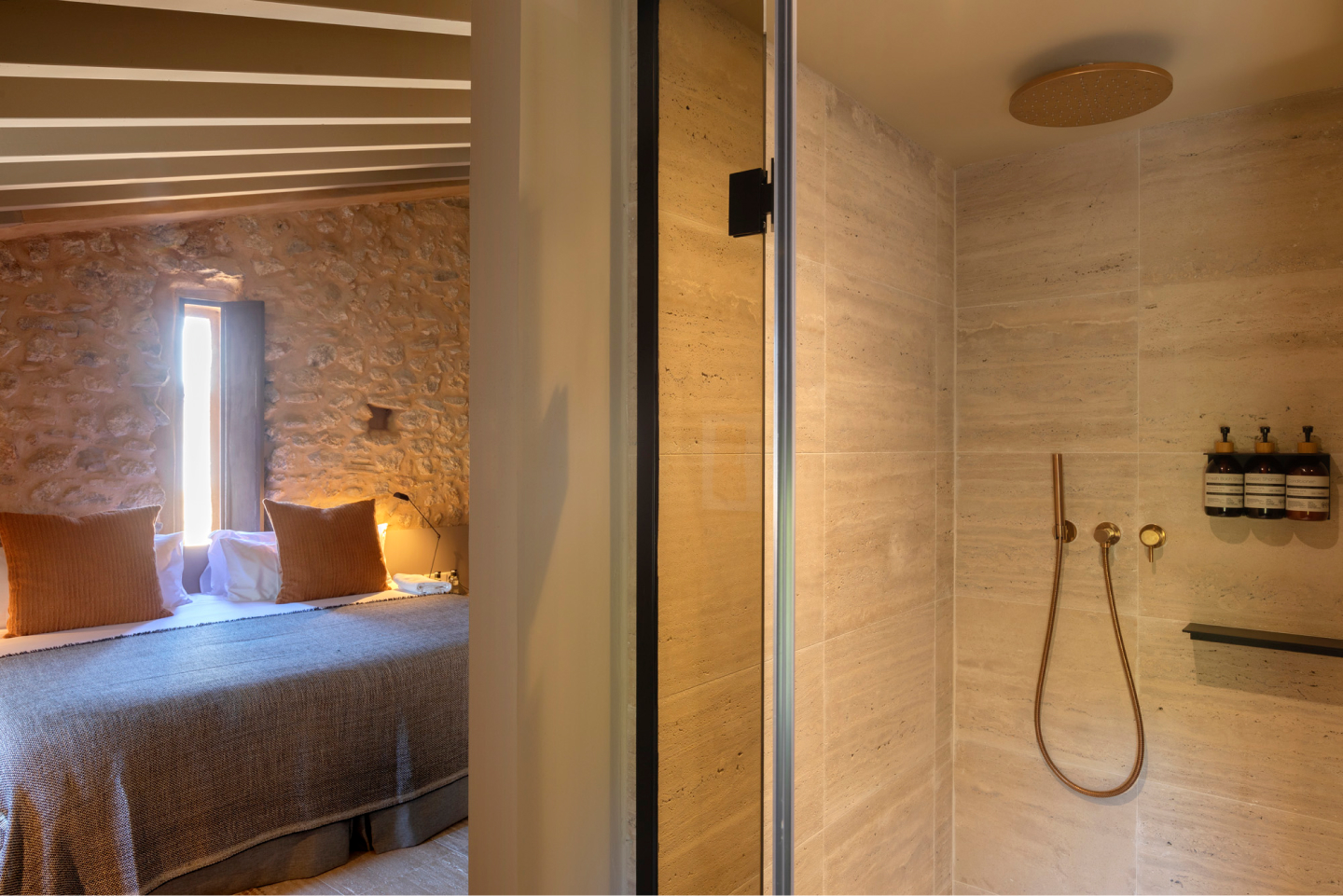 A bathroom in the same stone-and-linen language, a stone basin and warm-toned tile lit by a soft band of daylight